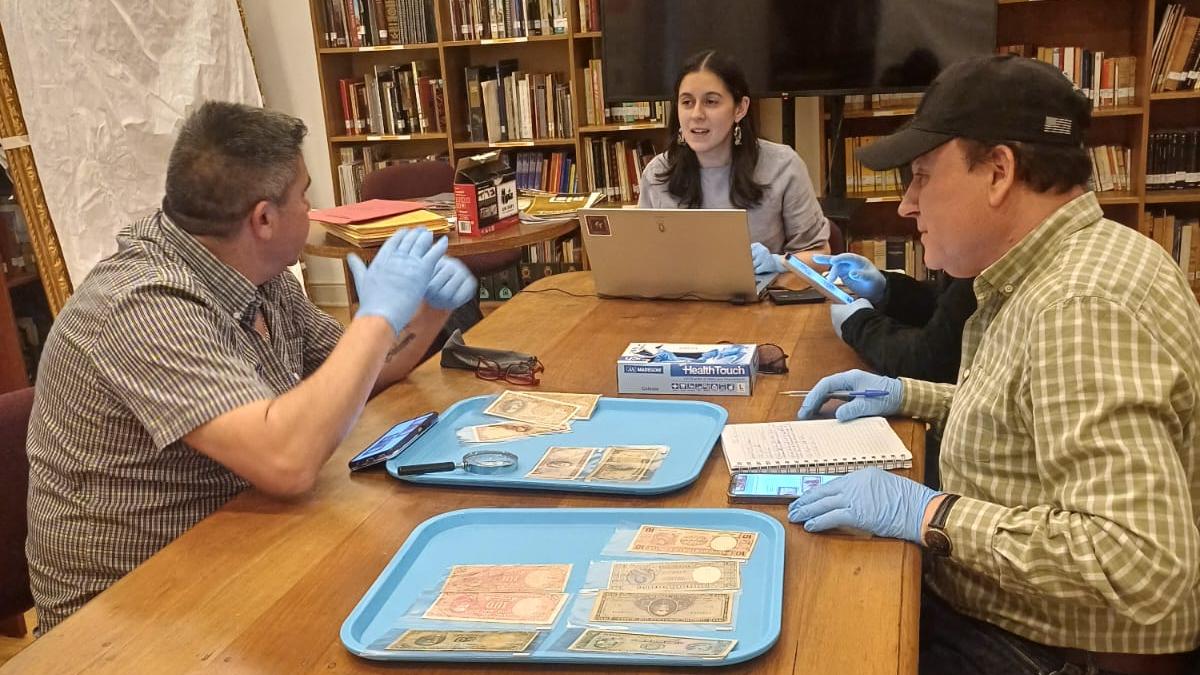 Cuatro personas sentadas alrededor de una mesa, sobre la cual se encuentran dos bandejas con billetes