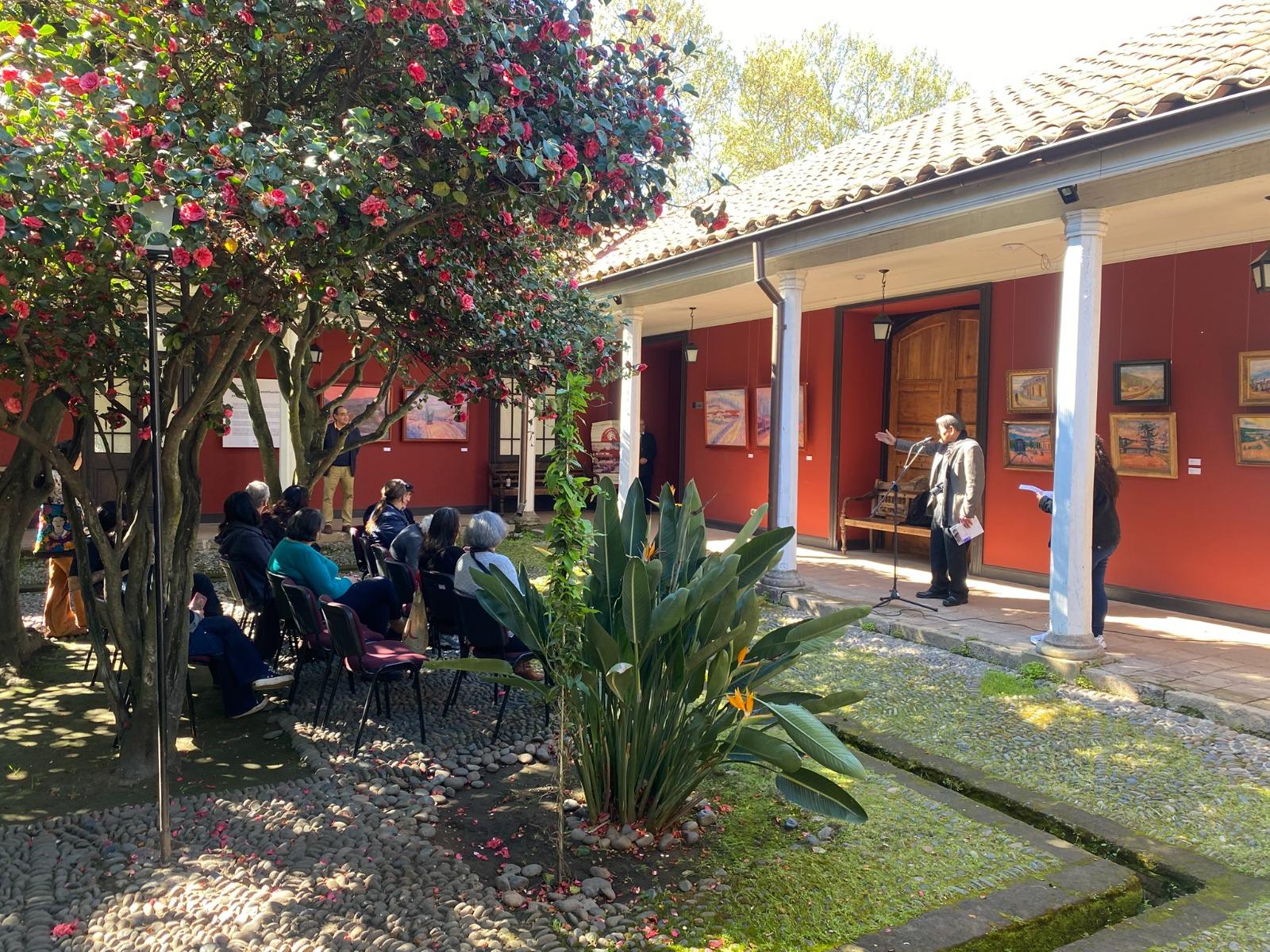 El pintor Hugo Pereira Núñez se dirige a un grupo de personas, sentadas, durante la inauguración de la exposición en un patio del museo