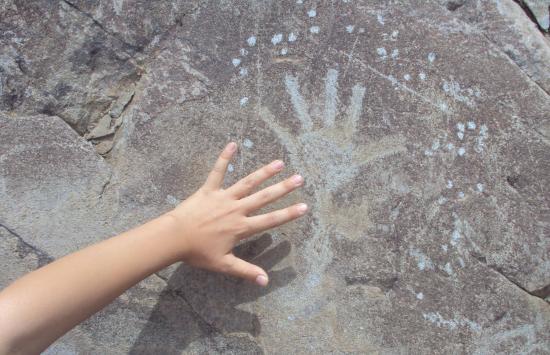Mano infantil que posa sobre la imagen de una mano tallada en una roca